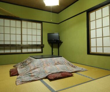 Traditional tatami room with futon, shoji screens, floor cushions and wall-mounted television at Warabiso in Niigata
