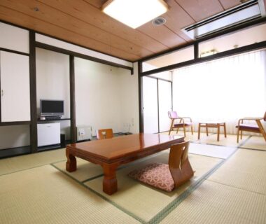 Spacious tatami room with low wooden table, floor cushions, sliding panels and window seating at Wasuki Tsukasakan, Kumamoto