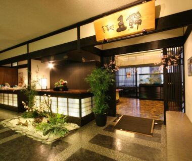 Ryokan reception area with wooden counter, decorative signboard, shoji screens and indoor stone flooring