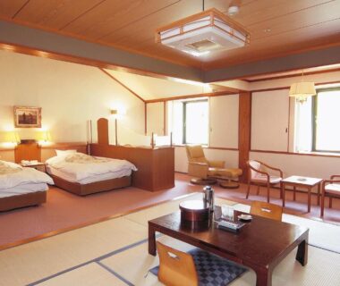 Spacious tatami room with low table, floor cushions and two beds at Watarase Onsen Hotel Sasayuri, Wakayama