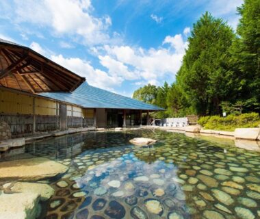 Outdoor onsen bath with stone bottom and wooden bathhouse at Watarase Onsen Hotel Yamayuri in Wakayama