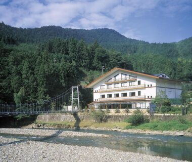 Riverside ryokan by a suspension footbridge with pebble riverbank and forested mountains in Wakayama, Japan