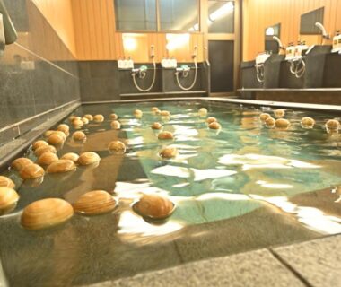 Indoor onsen bath with floating citrus fruits, tiled basin, wooden paneling and shower stations at Watazen Ryokan Kyoto