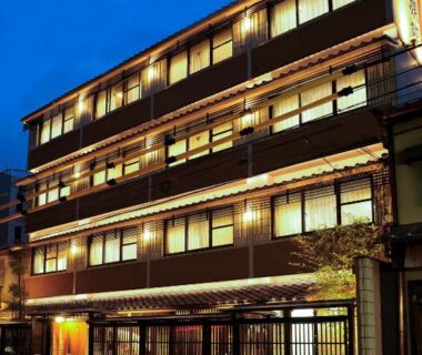 Evening exterior of multi-story Watazen Ryokan with warm lit windows and wooden lattice frontage in Kyoto Kansai