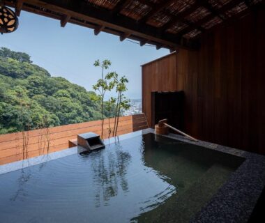 Covered stone onsen bath with wooden screen opening to forested hillside at Watei Kazekomichi Shizuoka