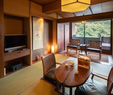 Tatami room with low table, chairs and balcony overlooking wooded hillside at Watei Kazekomichi, Shizuoka