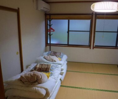 Tatami room with folded futons and cushions, sliding frosted windows at Wholeearth Ryokan Hiroshima, Chūgoku, Japan