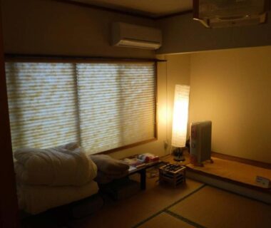 Cozy tatami room with folded futon, low table, floor lamp and shoji-style window at Wholeearth Ryokan Hiroshima