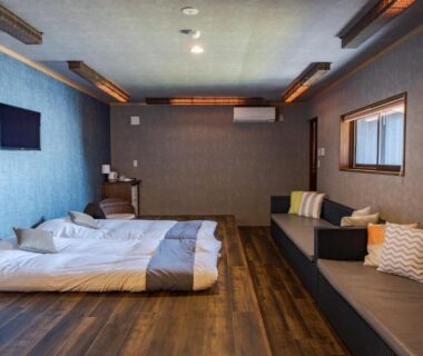 Two futons on wooden floor with low sofa seating, wall-mounted TV and window in a Wakayama ryokan room
