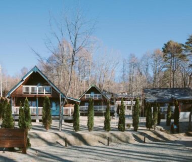 Wooden A-frame cottages with gravel courtyard and small evergreens at Yatsugatake Kogen Resort, Yamanashi