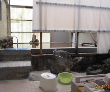 Indoor communal wash area with stools and stone bath at YOKOSO Ryokan in Ōita, Kyūshū