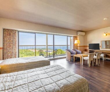 Twin beds, seating area and balcony with distant sea view, wood flooring at YU-FURI Izukogen in Shizuoka