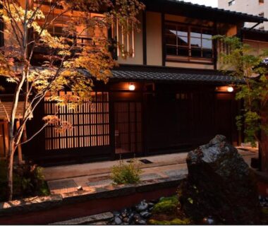Warmly lit wooden facade with stone path and shoji screens at Yado Kiramachi in Kyoto