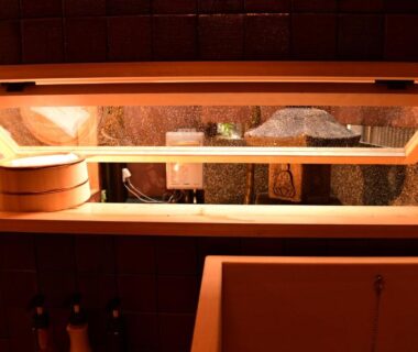 Warm-lit wooden soaking tub with bath bucket and window in ryokan bathroom