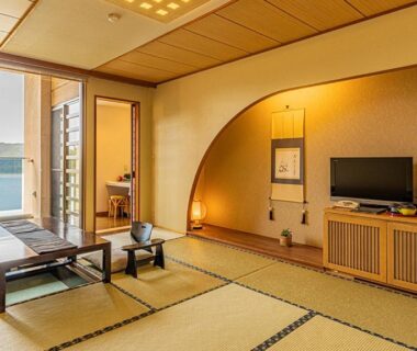 Tatami room with low table, tokonoma alcove and sliding doors revealing a coastal water view at Yado Marubun, Shizuoka