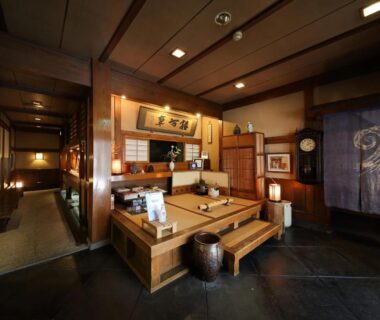 Traditional wooden reception with raised seating platform, lanterns, framed art and noren at Kyoto ryokan