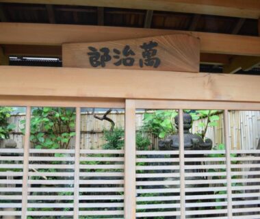 Traditional wooden slatted entrance with kanji sign and glimpse of garden at Yadoya Manjiro Kyoto