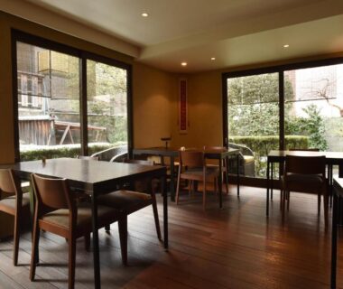 Dining room with wooden tables and chairs and large garden-facing windows at Yadoya Nishijinso, Kyoto