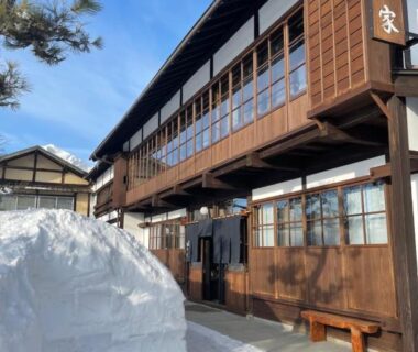 Traditional multi-story wooden facade of Yadoya Shiroganeya with snow drifts at entrance in Nagano