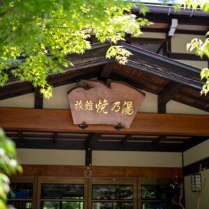 Wooden ryokan entrance with carved sign and green foliage at Yakenoyu in Gifu, Chūbu