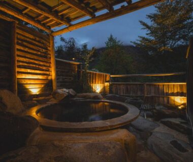 Stone outdoor onsen tub with wooden enclosure and lantern lighting at Yakenoyu, Gifu