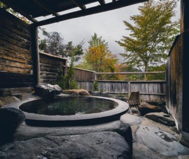 Round stone outdoor onsen with wooden fence and autumn foliage at Yakenoyu, Gifu, Chūbu, Japan