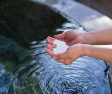 Hands cupping onsen water at a stone bath with gentle ripples