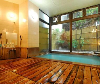 Indoor onsen bath with wooden deck, tiled wash stations and garden-facing windows at Yakushi no Yu Yumotokan in Gunma