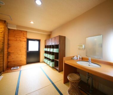 Tatami-floored changing area with sink, wooden shelves and baskets at Yama no Yado Meiji Onsen in Nagano