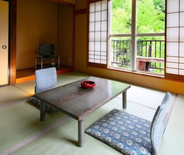 Tatami room with low table, floor cushions, shoji screens and veranda overlooking green trees