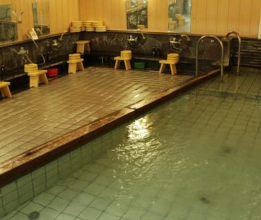 Indoor tiled onsen with wooden washing area, stools and faucets at Yamabiko, Nagano