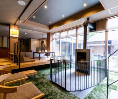 Ryokan lounge with central hearth, low wooden seating and garden-facing windows at Yamabiko in Nagano
