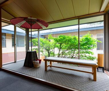 Veranda seating with wooden bench, traditional umbrella and courtyard greenery at Yamabiko Ryokan, Nagano