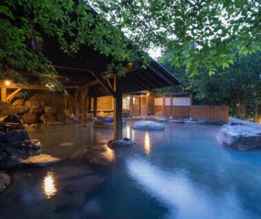 Covered outdoor onsen with rocks, timber shelter and soft evening lighting at Yamabiko Ryokan in Kumamoto