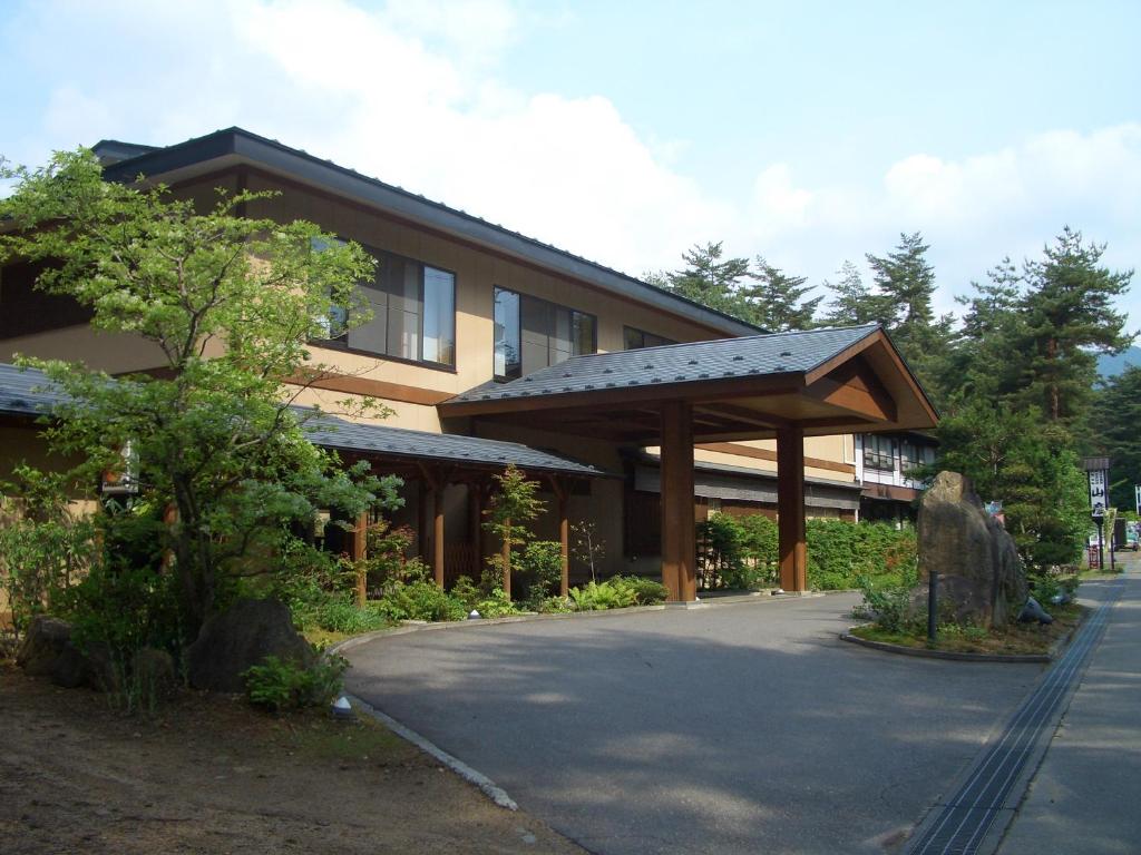 Entrance of Yamabiko Ryokan Nagano Chūbu Traditional two-story ryokan entrance with wooden portico, driveway and surrounding trees in Nagano's Chūbu region