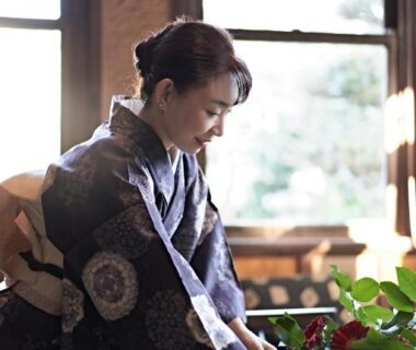 Woman in kimono arranging flowers by window at Yamada Bessou, Ōita ryokan