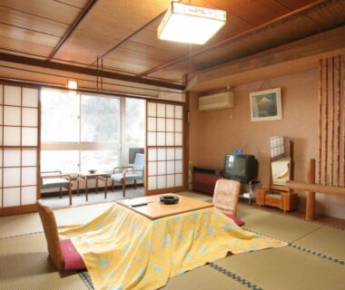 Tatami room with blanket-covered low table, floor chairs and shoji screens at Yamadaya Hotel in Yamanashi, Chūbu, Japan