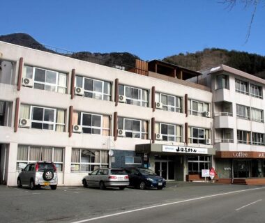 Three-story Yamadaya Hotel facade with parked cars and mountain backdrop in Yamanashi, Chūbu