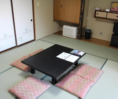 Traditional tatami room with low lacquered table, pink zabuton cushions and shoji sliding doors at Yamadaya Hotel in Yamanashi