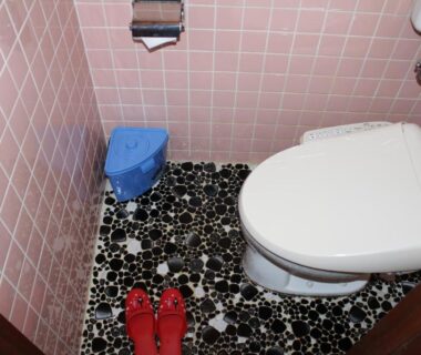Pink tiled restroom with patterned pebble floor, electronic bidet toilet seat and red slippers at Yamadaya Hotel Yamanashi