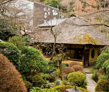 Traditional thatched-roof ryokan building with manicured moss garden and stone path at Yamagaso in Kanagawa