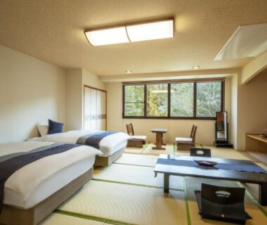 Tatami room with twin beds, low table, TV and windows overlooking trees at Yamagataya in Fukushima