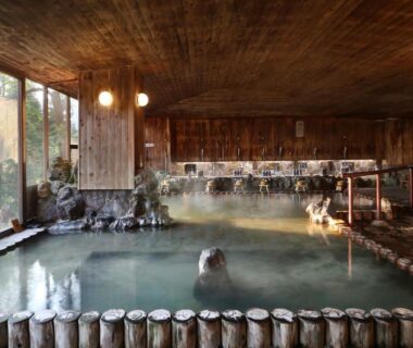Large indoor wooden onsen bath with rock features at Yamagataya Fukushima Tōhoku