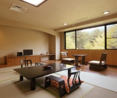 Spacious tatami room with low table, floor chairs and large window overlooking trees at Yamagataya, Fukushima