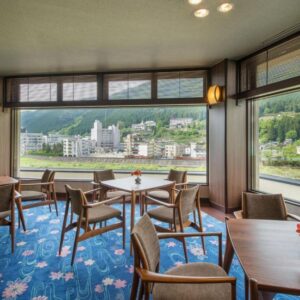 Seating area with tables and panoramic windows overlooking river and town at Yamagataya in Gifu, Chūbu region