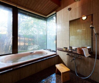 Indoor bathtub with shower and wooden stool at Yamaha Resort Katsuragi Kitanomaru, Shizuoka, overlooking trees