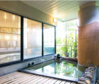 Wooden-deck indoor bath with stone tub and garden view at Yamaichi, Iwate