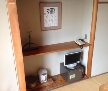 Tatami room alcove with wall scroll, low shelf, small TV, electric kettle, telephone and sliding door at Yamaichi Bekkan, Hiroshima