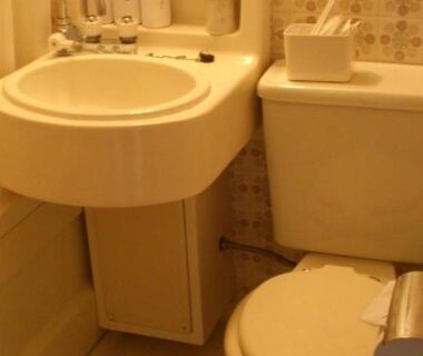 Compact ryokan bathroom with sink, toilet, wall-mounted toiletry dispensers and patterned wallpaper at Yamaichi Bekkan, Hiroshima