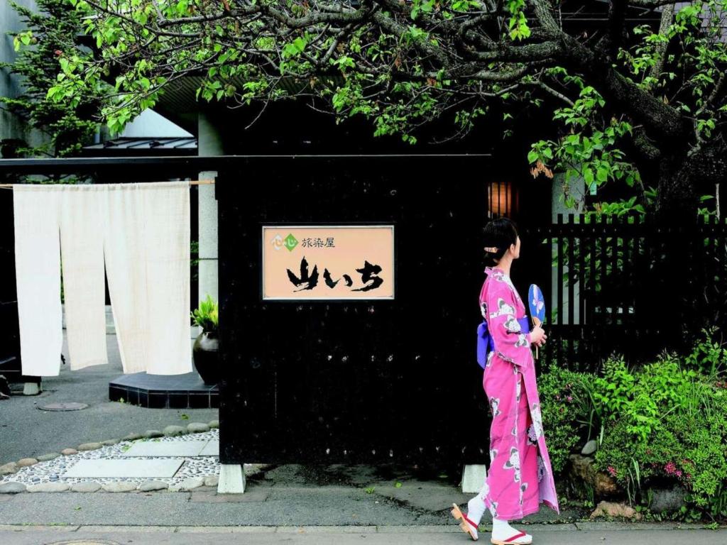 Guest in Yukata at Yamaichi Iwate Person in pink yukata walking past Yamaichi entrance with noren and wooden gate in Iwate